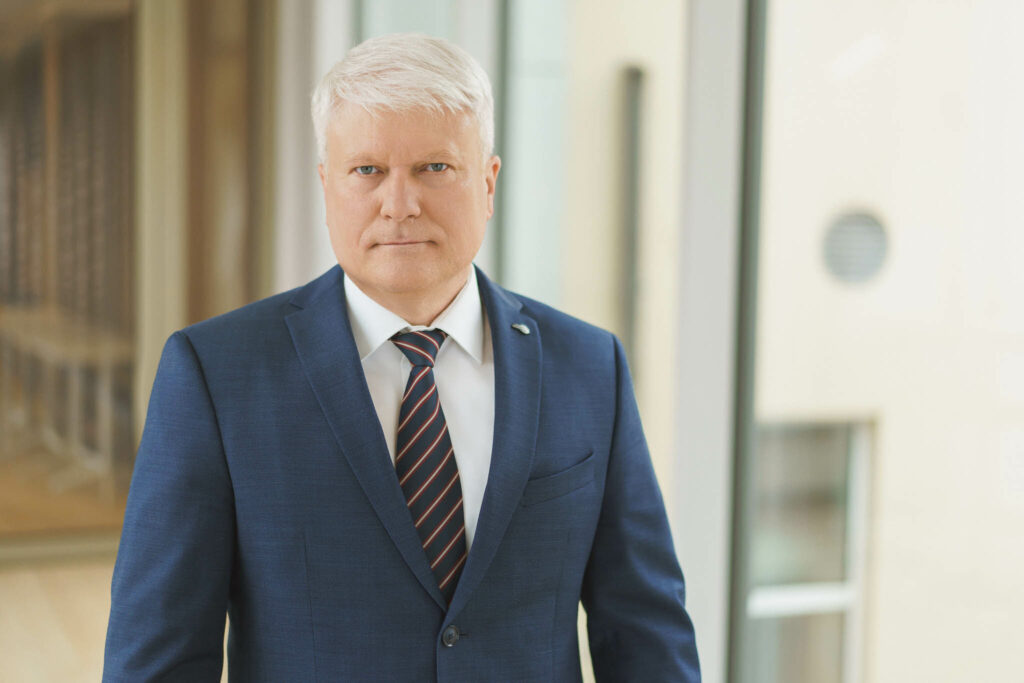 Žilaplaukis vyras mėlynu kostiumu ir dryžuotu kaklaraiščiu.