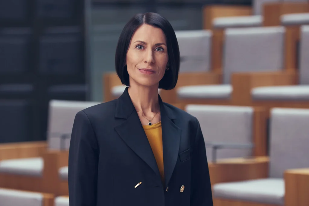 Aušrinė Armonaitė, politikė, tamsiu kostiumu, konferencijų salės fone.