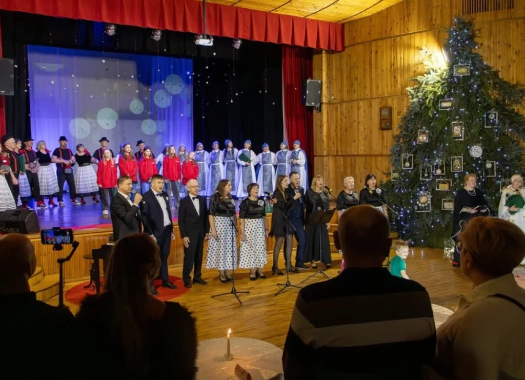 Kalėdiniame koncerte choras dainuoja prie didelės eglės, papuoštos rėmintais laikrodžiais, pilnoje atlikėjų scenoje.