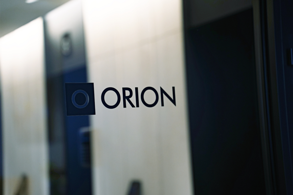 „Orion“ bendrovės logotipas ant stiklinių biuro durų.