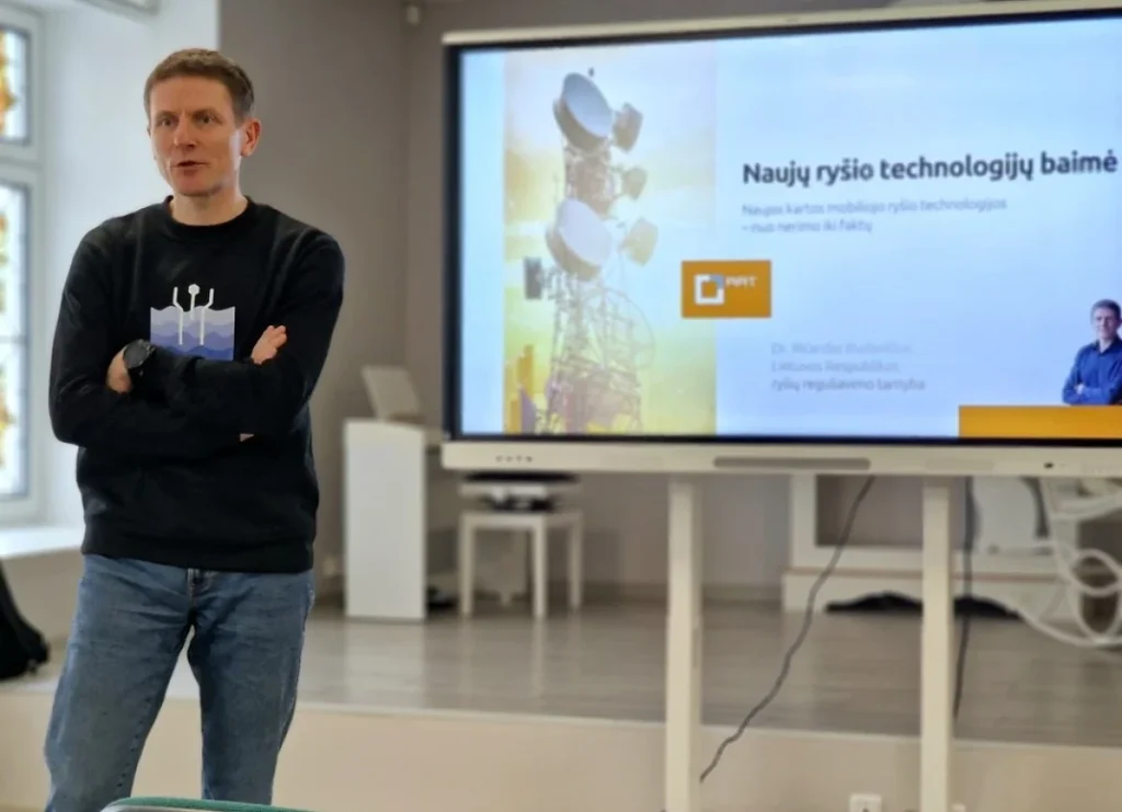 Vyras stovi prie ekrano, kuriame rodoma skaidrė apie naujų ryšio technologijų baimę ir faktus.