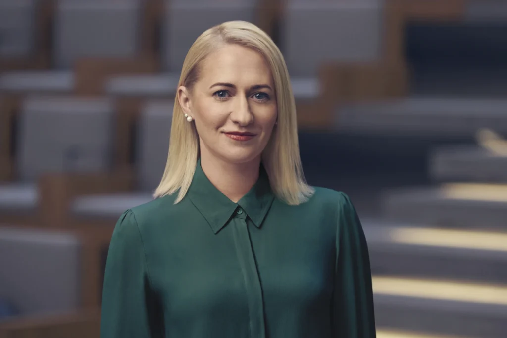 Jurgita Šiugždinienė dėvinti žalią palaidinę auditorijos fone.