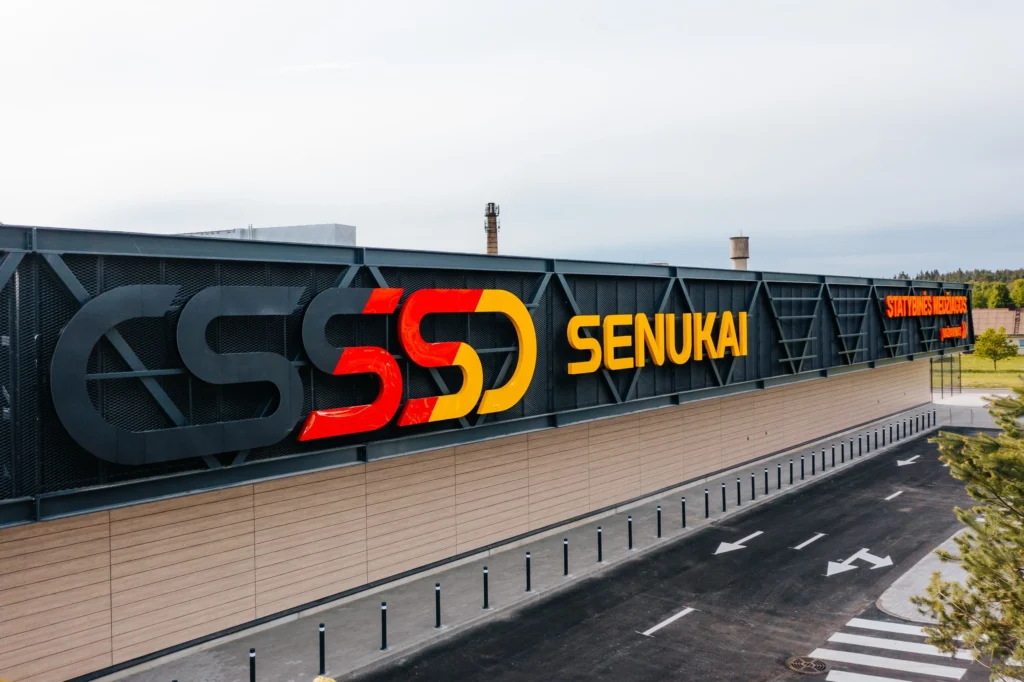 Didelė parduotuvės „Senukai“ iškaba ant modernaus pastato pilko fasado.