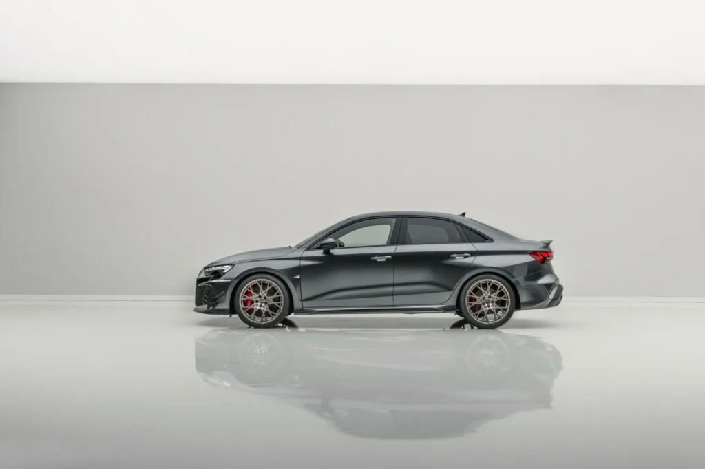 Pilkas sportinis „Audi“ sedanas šviesioje studijoje iš šono.