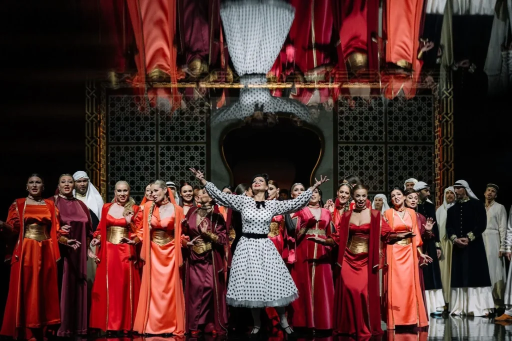Operos solistė taškuota suknele ir aktorių trupė scenoje.