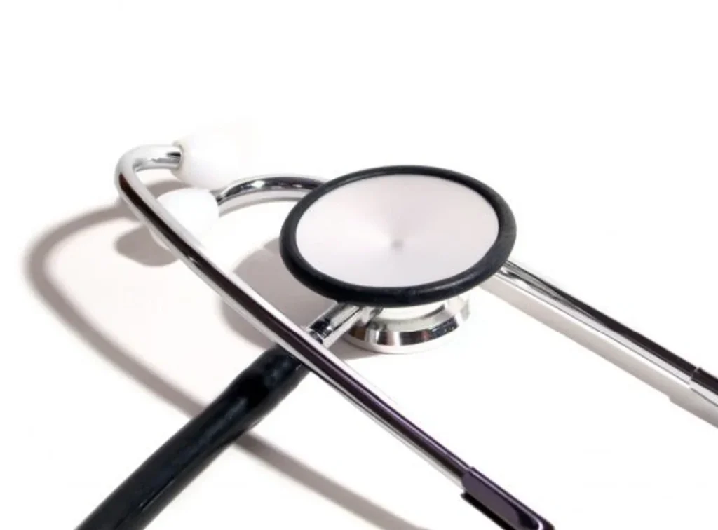 Medicininis stetoskopas su juodais laidais ir metalinėmis detalėmis padėtas ant balto fono.