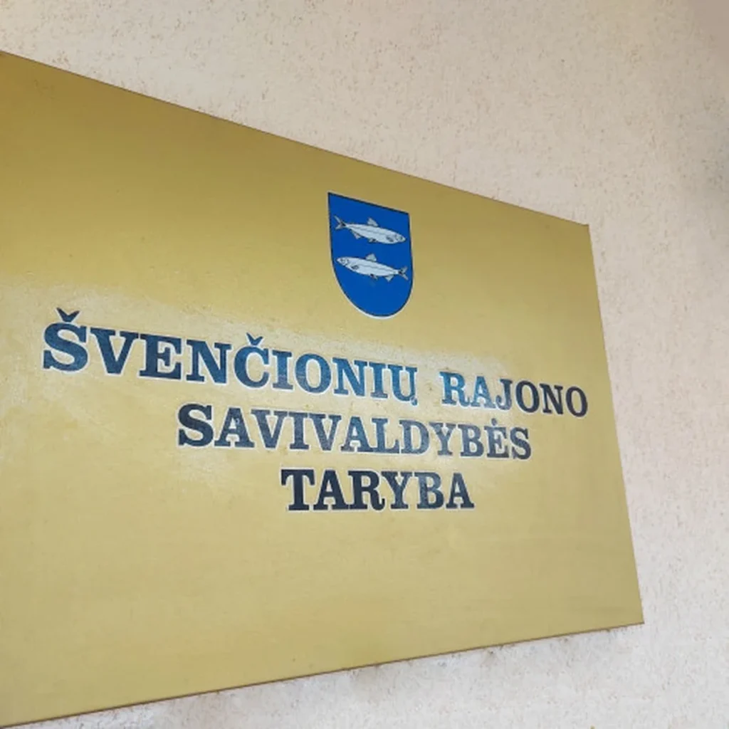 Auksinė lentelė su užrašu Švenčionių rajono savivaldybės taryba ir mėlynu herbu su dviem žuvimis.