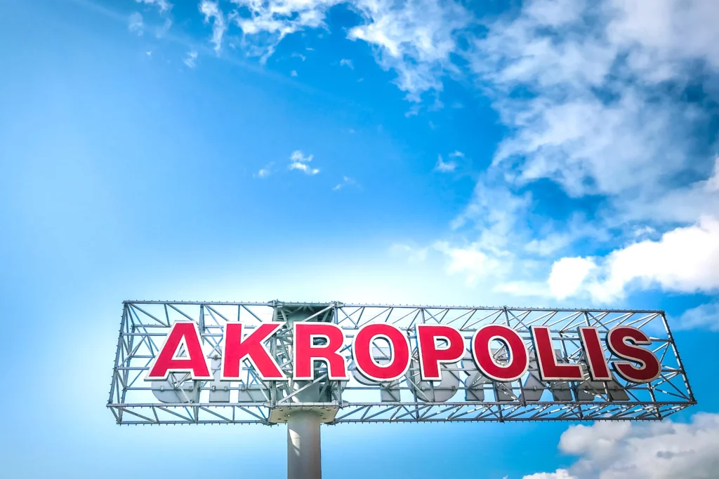 Didelis raudonas prekybos centro „Akropolis“ užrašas mėlyno dangaus fone.
