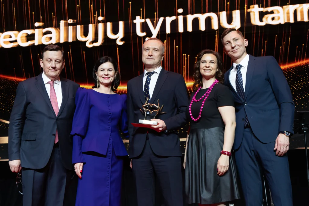 Penki oficialiai apsirengę asmenys scenoje su gautu apdovanojimu.