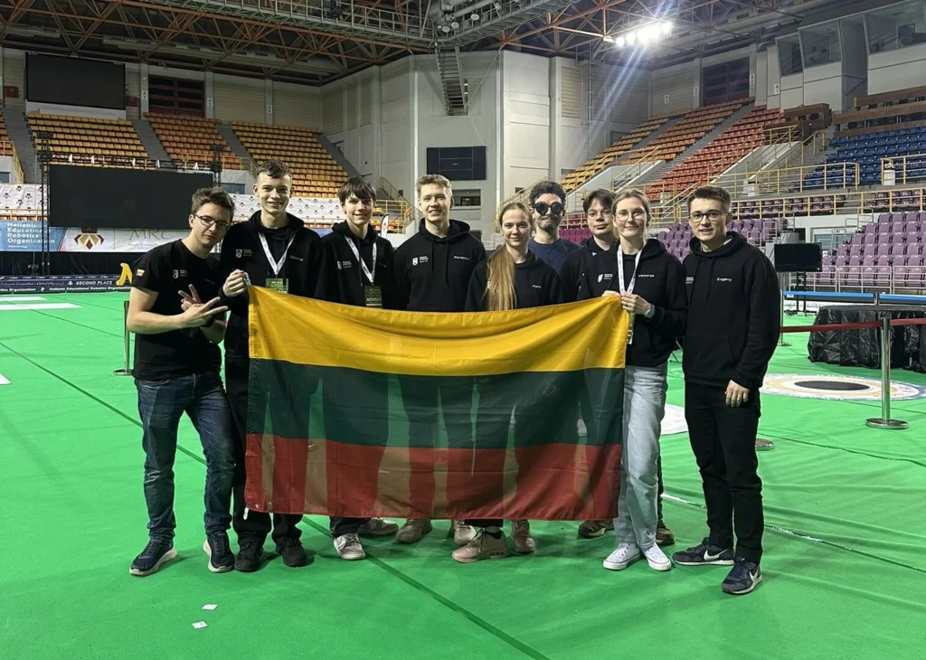 Grupė jaunuolių laiko Lietuvos vėliavą didelėje sporto arenoje.