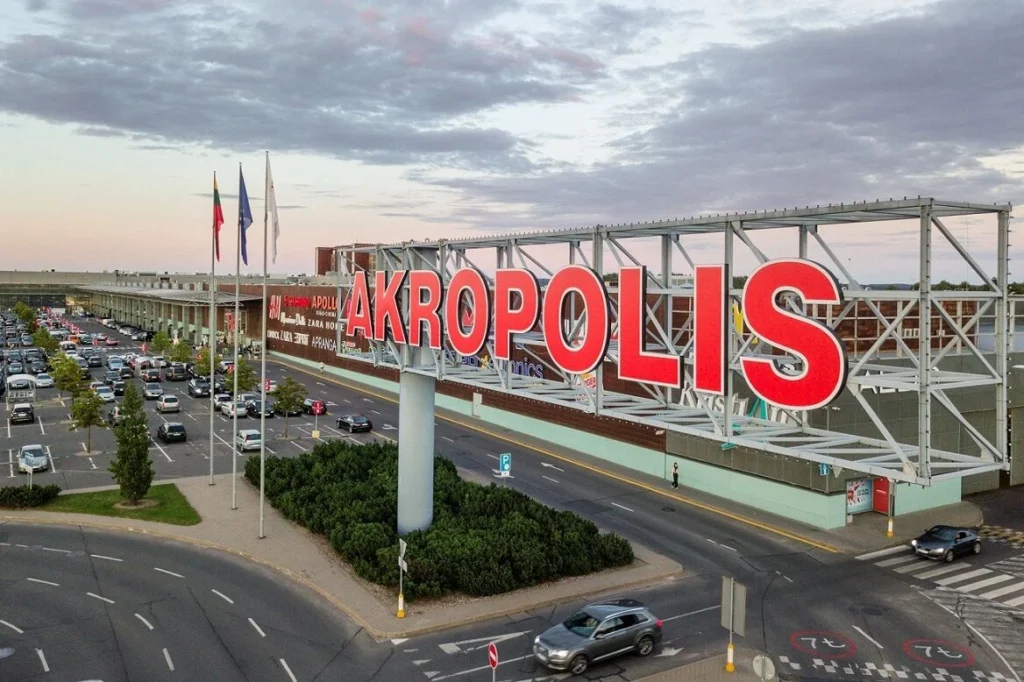 Didelis raudonas užrašas „Akropolis“ prie prekybos centro aikštelės.