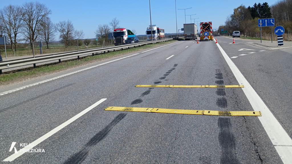 Geltoni greičio mažinimo kalneliai kelyje šalia kelio priežiūros transporto.