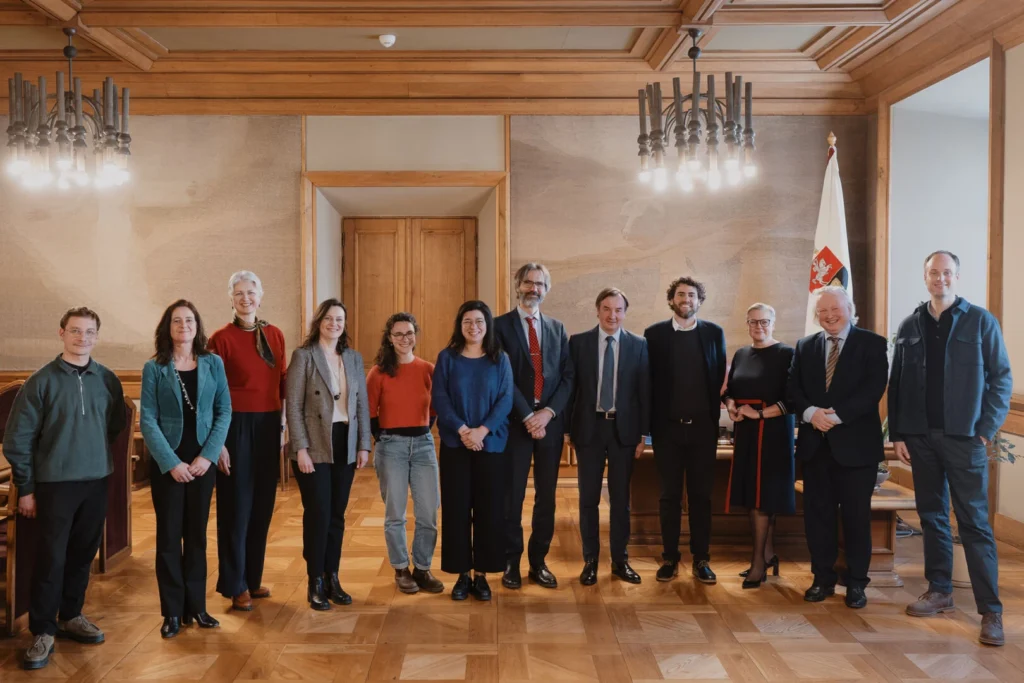 Ingrida Šimonytė ir grupė žmonių stovi oficialioje salėje.