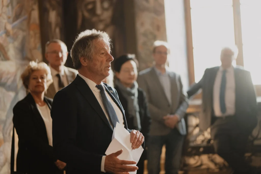 Kostiumuotas vyras sako kalbą oficialaus renginio metu.