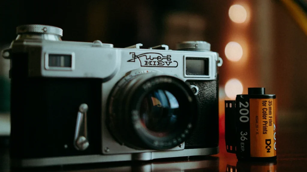 Klasikinis fotoaparatas „Kiev“ ir kino juostelė ant tamsaus fono, simbolizuojantys tradicinę kino estetiką