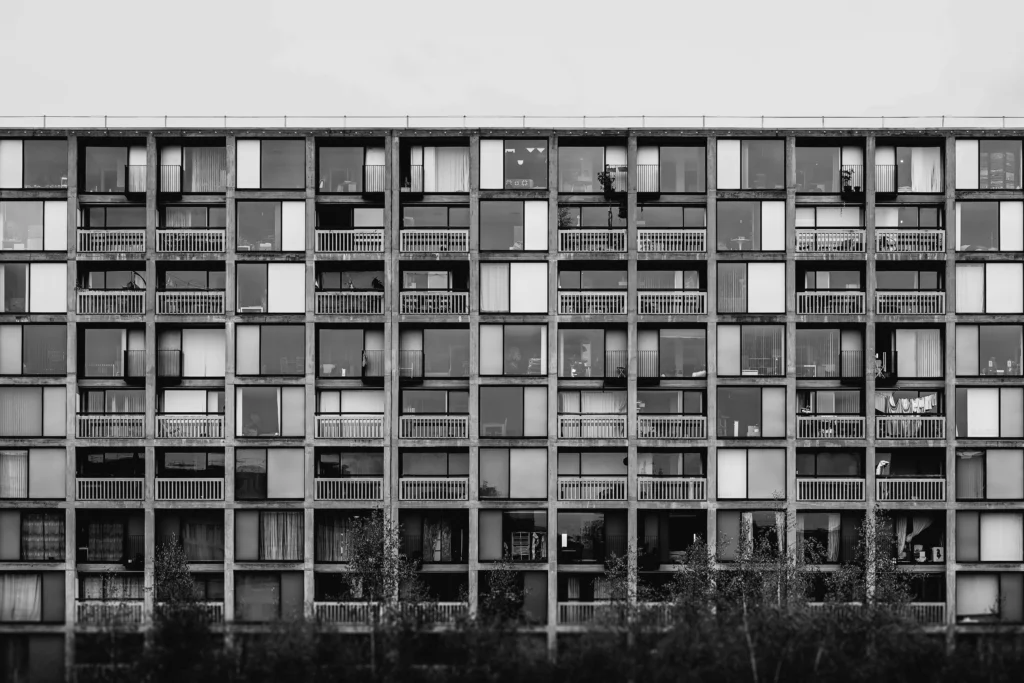 Juodai balta nuotrauka, vaizduojanti ritmišką modernaus daugiabučio fasadą su simetriškais langais ir balkonais.