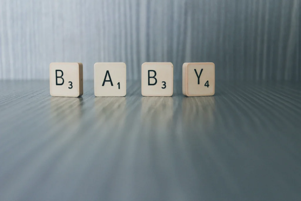 Keturios medinės žaidimo kaladėlės su raidėmis sudėlioja anglišką žodį „BABY“ ant pilko tekstūrinio paviršiaus.