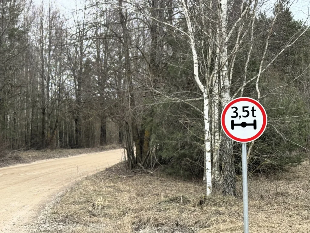 Kelio ženklas, ribojantis ašies apkrovą iki 3,5 tonos, stovi pamiškėje šalia vingiuoto žvyrkelio.