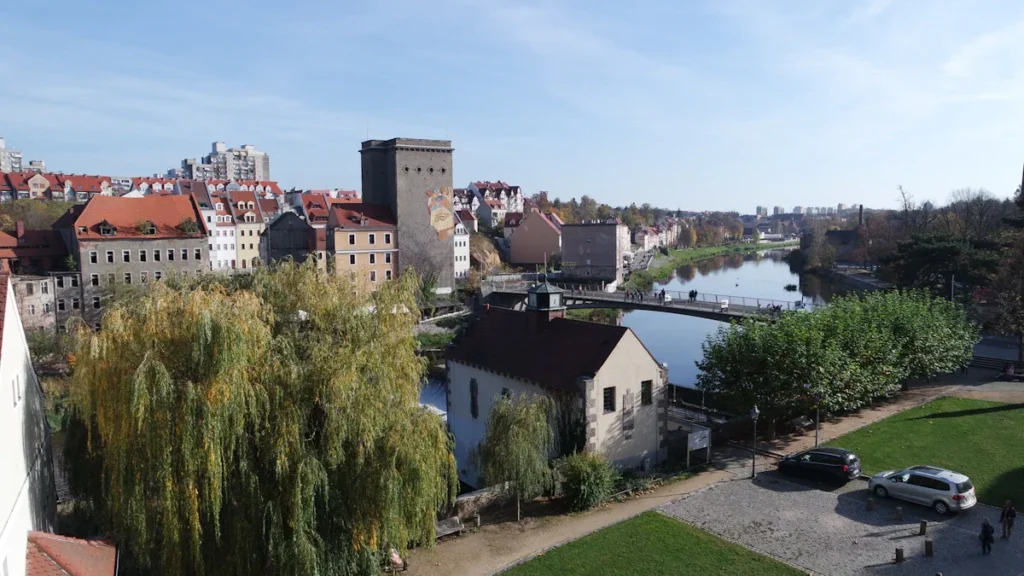 Miesto panorama su upės vaga, tiltu ir senamiesčio architektūra po giedru dangumi.
