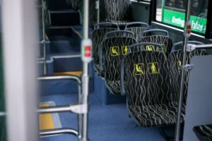 Tuščios modernaus autobuso sėdynės su geltonais piktogramų ženklais prioritetinėms keleivių grupėms.