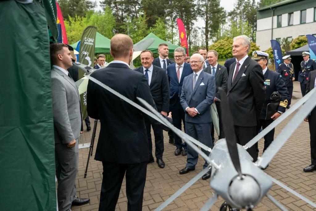 Prezidentas Nausėda ir Švedijos karalius apžiūri karinį droną kartu su delegacija lauko renginyje.
