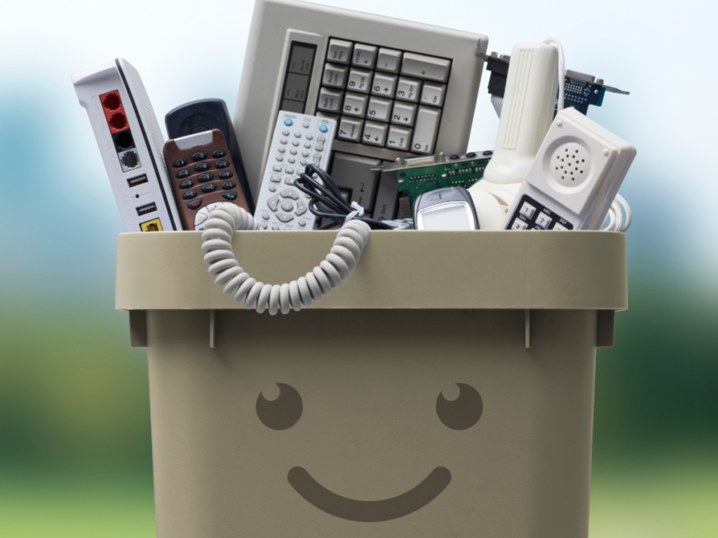 Besišypsanti dėžė, pilna senų elektronikos prietaisų: klaviatūros, pultelių, maršrutizatoriaus ir telefono dalių.