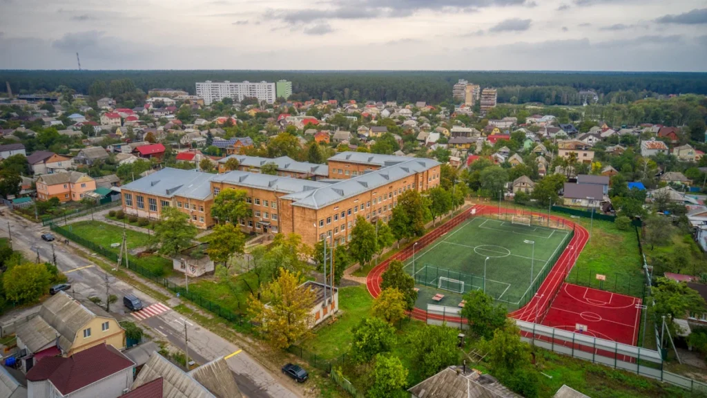 Iš viršaus nufotografuotas atnaujintas mokyklos stadionas su bėgimo takais ir sporto aikštynais gyvenamajame rajone.