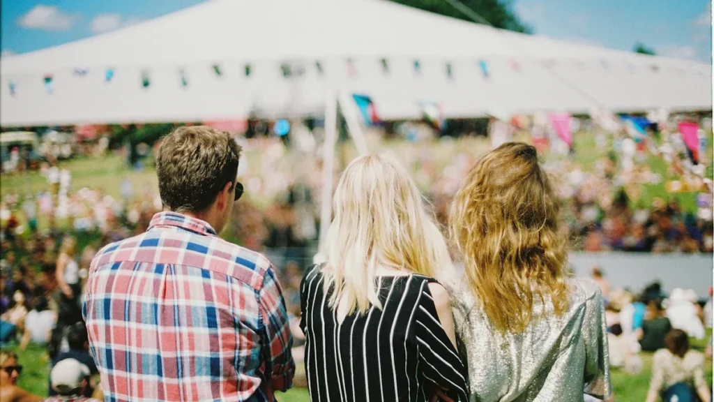 Jauni žmonės stebi vasaros muzikos festivalį po atviru dangumi saulėtą dieną.