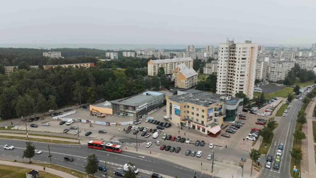 Iš oro matomas Vilniaus rajonas su automobilių stovėjimo aikštele, pastatais ir judria miesto gatve.
