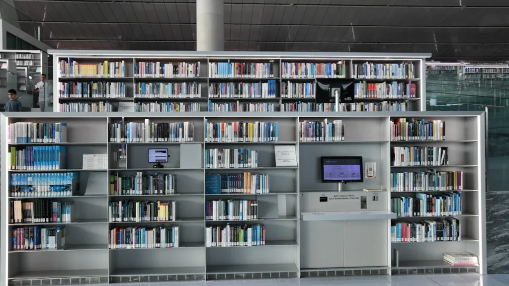 Modernios bibliotekos lentynos su knygomis šviesioje, erdvioje miesto skaityklos aplinkoje.