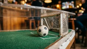 Mažas futbolo kamuolys ant stalo futbolo stalo su vartais ir žalia danga.