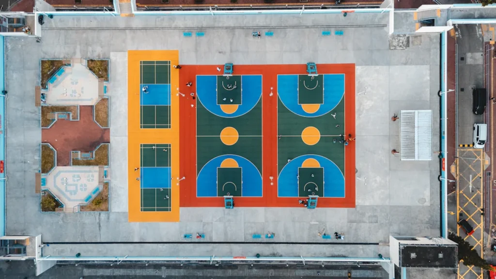 Spalvingi lauko krepšinio ir teniso aikštynai fotografuoti iš viršaus urbanistinėje aplinkoje