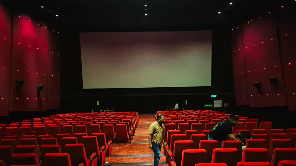 Tuščia kino teatro salė su raudonomis kėdėmis ir dideliu ekranu pasiruošusi seansui.