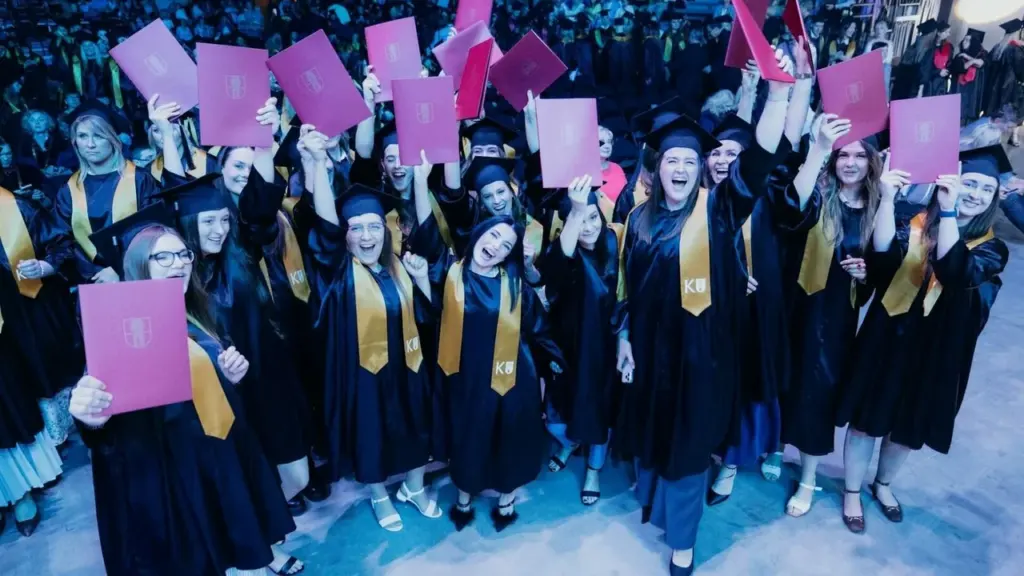 Džiugūs absolventai su mantijomis kelia į viršų diplomų įdėklus universiteto išleistuvių šventės metu.