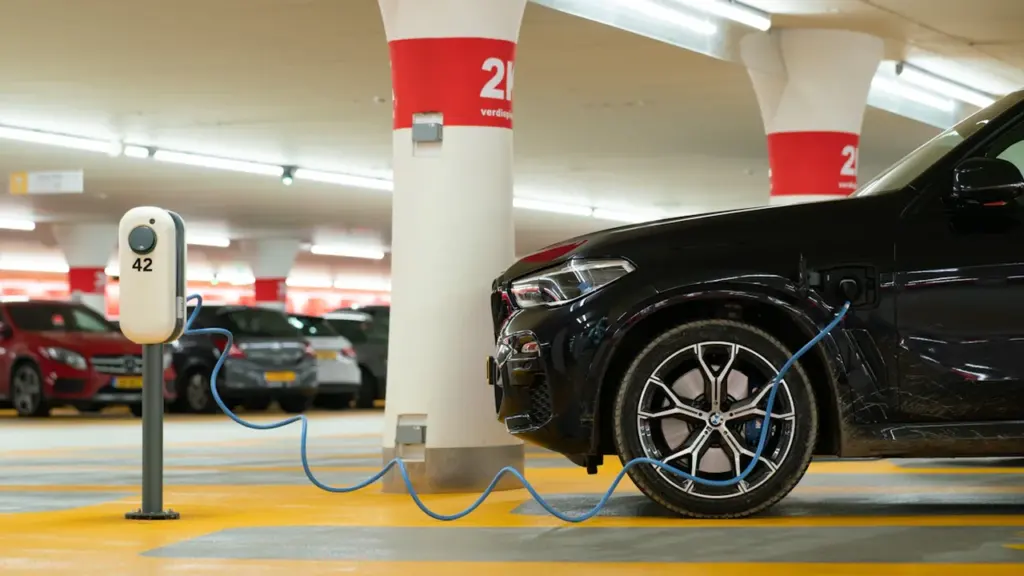 Elektromobilis kraunamas viešoje įkrovimo stotelėje modernioje požeminėje automobilių stovėjimo aikštelėje.