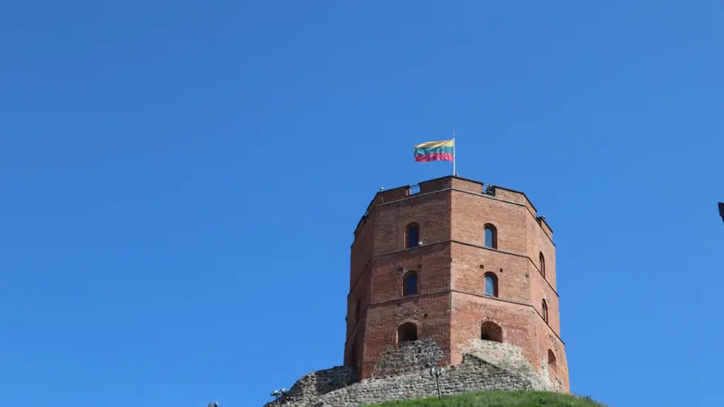 Gedimino bokštas su Lietuvos vėliava žaliame kalne po giedru vasaros dangumi