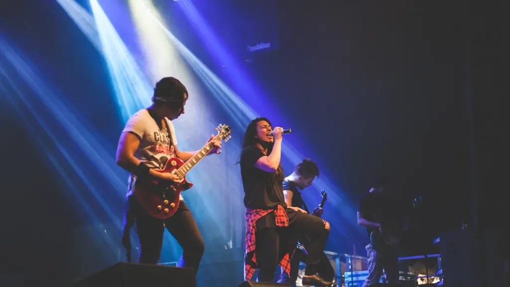 Muzikos grupė koncertuoja scenoje su apšvietimu didelės auditorijos renginio metu.