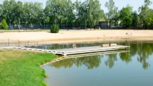 Prienų miesto parko tvenkinys su tilteliu ir sutvarkyta poilsio zona vasaros metu.