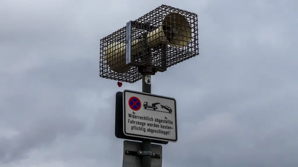 Garsinis sirenos signalas sumontuotas ant stulpo su informaciniais ženklais viešoje erdvėje.