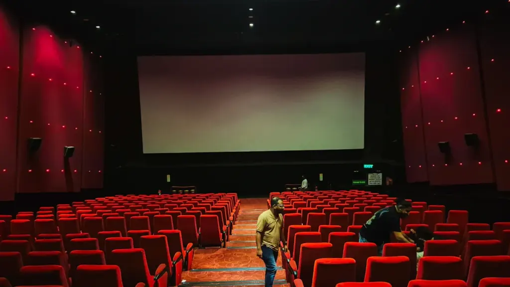 Tuščia kino salė su raudonomis kėdėmis ir dideliu ekranu prieš seansą.