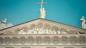 Didysis baltas katedros frontonas su skulptūromis ir kryžiumi, simbolizuojantis istorinę atmintį Lietuvoje.