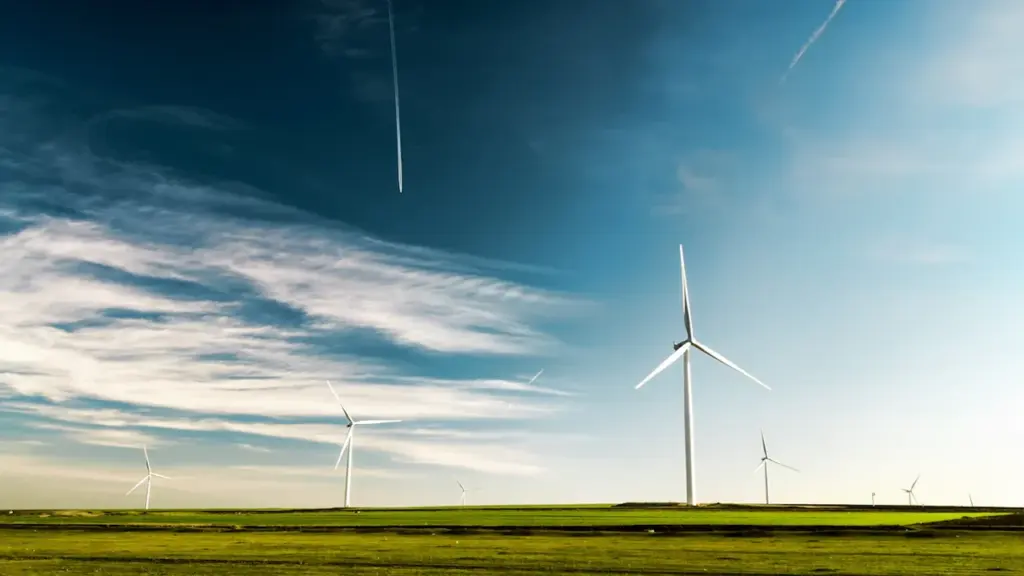 Vėjo jėgainės žaliuojančiame lauke su plačiu dangumi, atspindinčios atsinaujinančios energetikos plėtrą Lietuvoje.