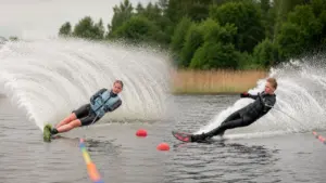 Du sportininkai vandens slidėmis skrodžia ežero paviršių, sukeldami didžiulius vandens purslus ir bangas.