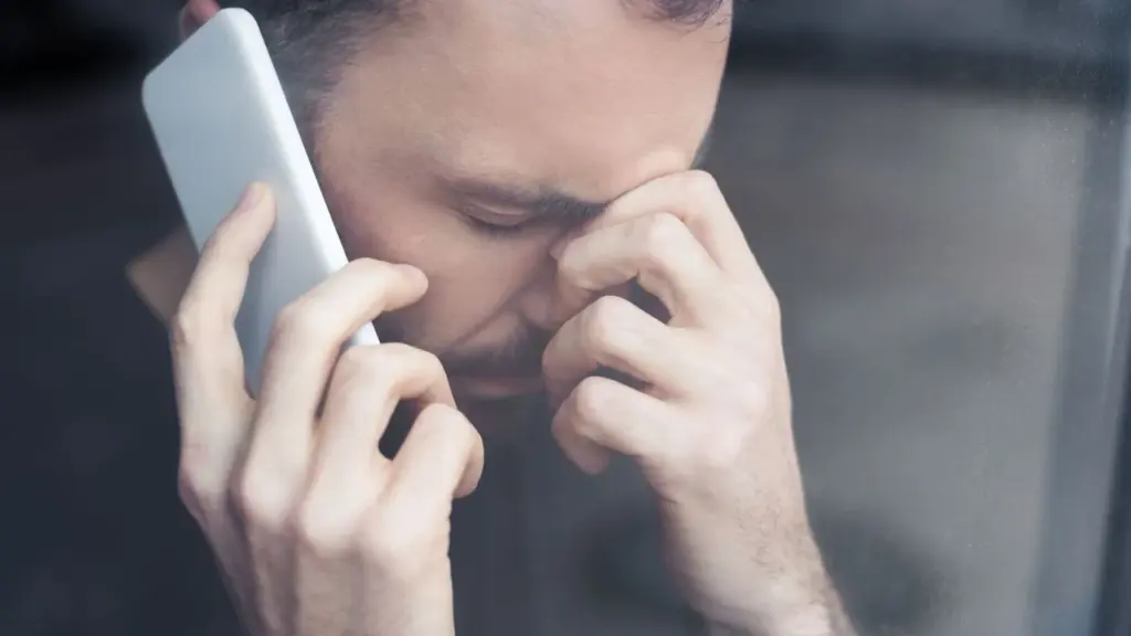 Vargstantis vyras laiko telefoną prie ausies ir susirūpinęs spaudžia smilkinius ranka.