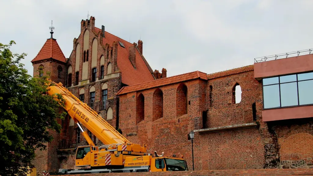 Gelinis statybinis kranas šalia raudonų plytų istorinio pastato Klaipėdos senamiestyje.