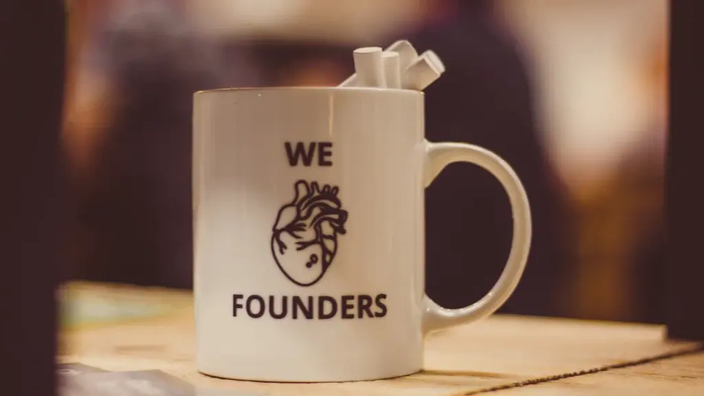 Keraminis puodelis su užrašu „We Founders“ ir širdies iliustracija ant medinio stalo