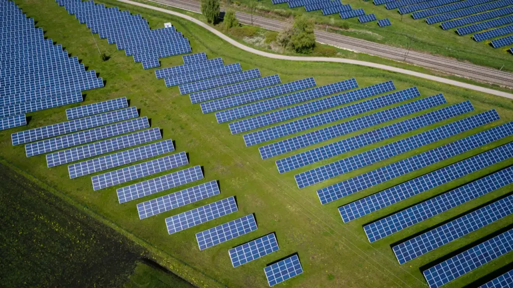 Saulės elektrinių parkas Lietuvoje – vaizdas iš paukščio skrydžio, saulės moduliai pievoje.