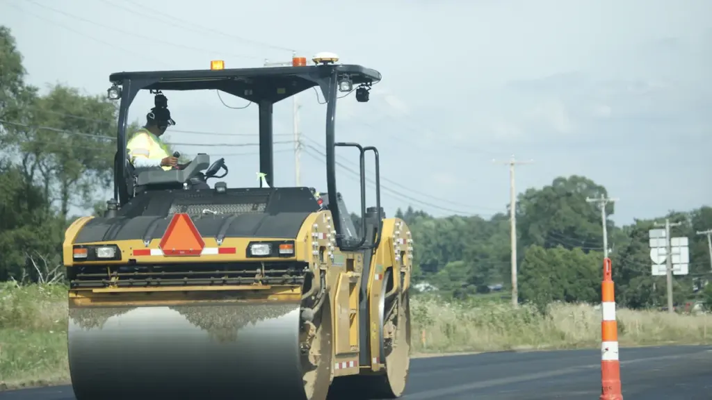 Sunkioji kelių tiesimo technika atlieka asfalto klojimo darbus kelyje šviesią dieną.