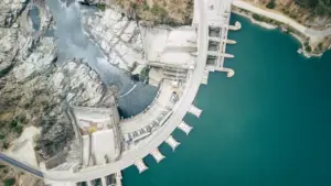 Iš oro fotografuota betoninė užtvanka ir šalia telkšantis gilus vandens telkinys.