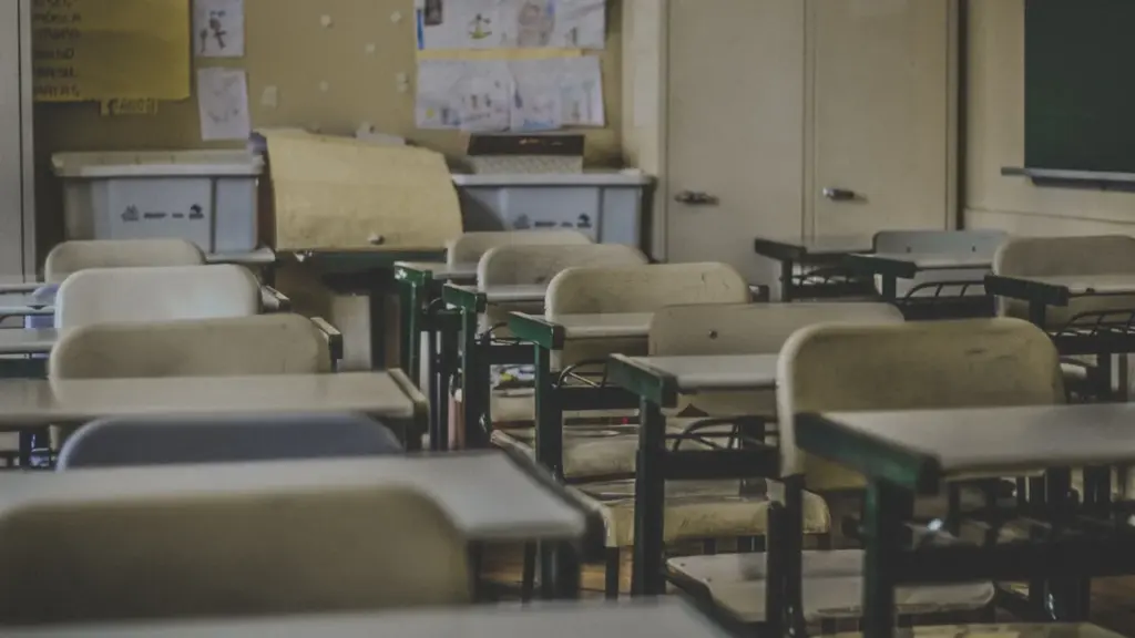 Tukščia mokyklos klasė su suolais, simbolizuojanti mažėjantį mokinių skaičių ir pokyčius gimnazijose.